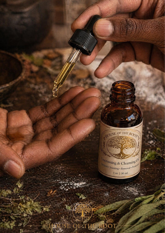 Hands applying Uncrossing and Cleansing Oil from a dropper with amber bottle, herbs, and ritual setup in warm lighting